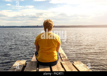 Un uomo si siede su un molo in legno e guarda al mare Foto Stock