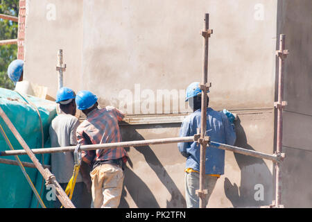 Una vista ravvicinata dei lavoratori in un cantiere in piedi sul ponteggio intonacatura di una nuova parete Foto Stock