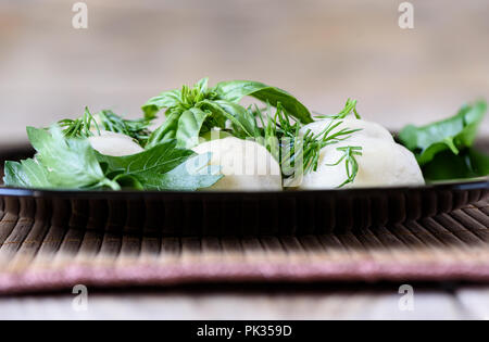 Gnocchi bolliti su una piastra con aneto, basilico e prezzemolo Foto Stock