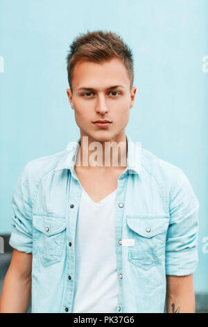 Close-up ritratto di una giovane ragazzo elegante in una camicia di denim in prossimità di una parete di blu. Foto Stock