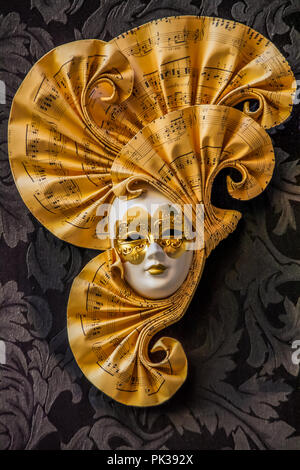 Un Dorato maschera veneziana, con una decorazione volute con un motivo musicale. Foto Stock