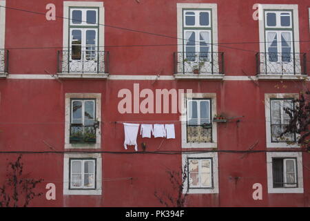 Rosso scuro facciata di una vecchia casa mediterranea in Portogallo, biancheria bianca pendente da una linea tra le finestre con infissi bianchi. Foto Stock