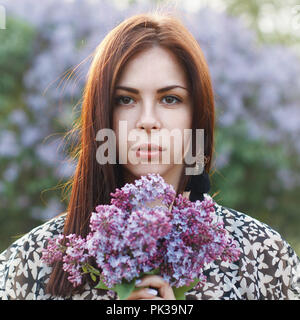 Bella ragazza tenendo un fiori lilla. Ritratto all'aperto. Foto Stock