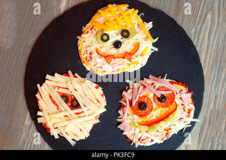 Raw pizza Halloween con mostri, al di sopra della scena con decor e su una piastra nera a prepararsi per cotto al forno, idea per la casa parte cibo, facile, sana e deliziosa fu Foto Stock