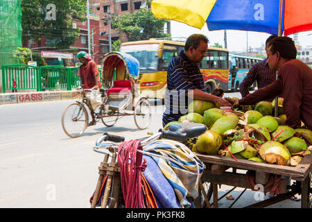 Un venditore ambulante di vendita noci di cocco fresco come un risciò ciclo passa in background sulla strada a Dhaka, nel Bangladesh. Foto Stock