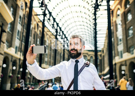 Imprenditore il trian Station di Londra, smorfie e tenendo selfie. Foto Stock