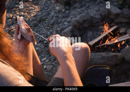 Donna riscaldamento hot dog vicino al fuoco Foto Stock