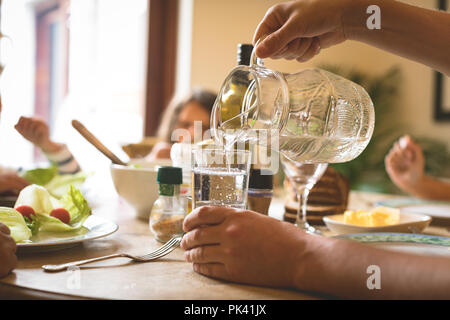 Uomo di servire acqua in vetro sul tavolo da pranzo Foto Stock