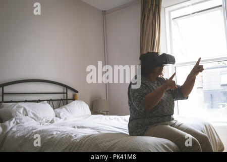 Senior donna utilizzando la realtà virtuale auricolare in camera da letto Foto Stock