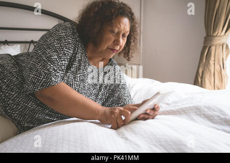 Donna senior con tavoletta digitale sul letto in camera da letto Foto Stock