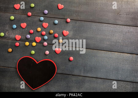 Amore romantico. A forma di cuore ad blackboard e caramelle su uno sfondo di legno, vista dall'alto e copia di spazio. Foto Stock