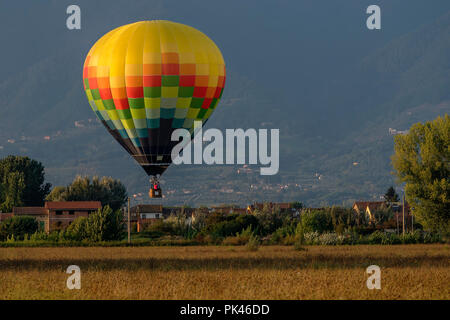 Coloratissima mongolfiera vola sopra tipico villaggio nella campagna toscana nella luce del tramonto Foto Stock