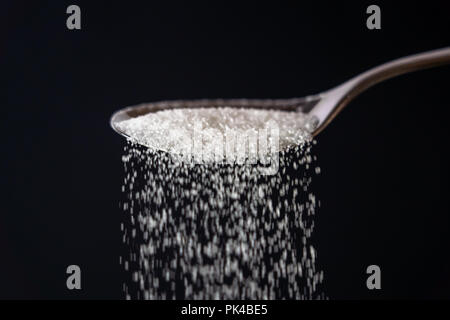 Studio Immagine di un metallo cucchiaio zucchero versatore isolata su uno sfondo nero in cucina dolce zucchero dipendenza malsana dieta sovrappeso e obesità co Foto Stock