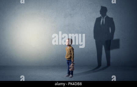 Little Boy immaginare che egli sarà uomo d affari e illustrando il suo futuro in una grande ombra Foto Stock