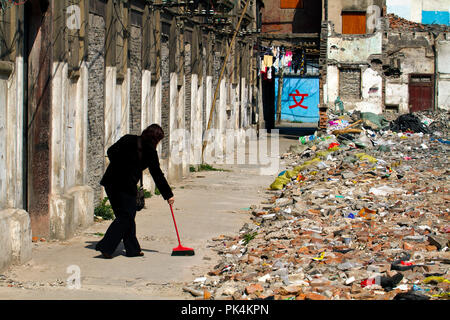 Spazzare il percorso tra le macerie delle case demolite. La vita di strada nel distretto di Luwan, Shanghai, Cina. Foto Stock