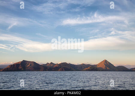 Sun si elevano al di sopra di un drammatico paesaggio di Komodo. Foto Stock