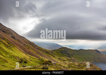 Le splendide vedute guardando fuori attraverso la campagna del Welsh come ho salito Mount Snowdon. La Moody nuvole aggiunto al suggestivo paesaggio. Foto Stock