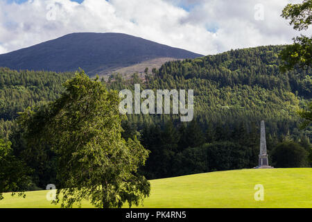 Memorial obelisco su di una collina con la foresta dietro e Mourne Mountains in distanza. Tollymore Forest Park, Newcastle, N.Irlanda. Foto Stock