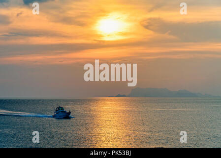 Il motoscafo per la pesca sul mare di ritornare a Riva durante il tramonto in mezzo alla natura e il bellissimo cielo. Foto Stock