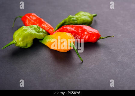 Rosso Verde e giallo peperoni fantasma su una superficie scura Foto Stock