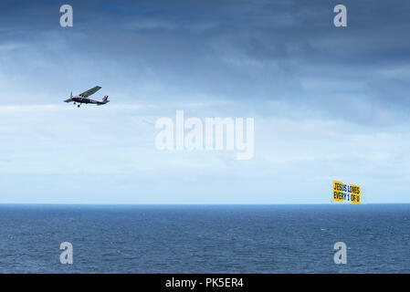 Un piccolo aeroplano volare sopra il mare e il traino di un banner con un messaggio religioso. Foto Stock