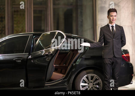 Chauffeur apertura porta auto per il trasporto di passeggeri Foto Stock