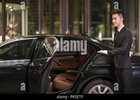 Chauffeur apertura porta auto per il trasporto di passeggeri Foto Stock