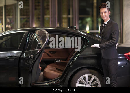 Chauffeur apertura porta auto per il trasporto di passeggeri Foto Stock