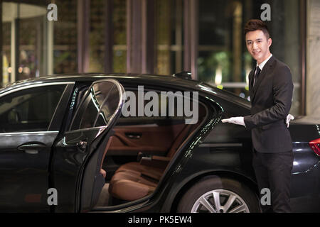 Chauffeur apertura porta auto per il trasporto di passeggeri Foto Stock