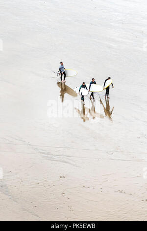 Una vista aerea di surfers e loro surf istruttore portando le loro tavole da surf dopo una lezione di surf. Foto Stock