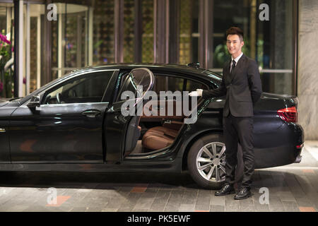 Chauffeur apertura porta auto per il trasporto di passeggeri Foto Stock