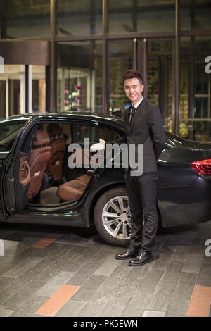 Chauffeur apertura porta auto per il trasporto di passeggeri Foto Stock