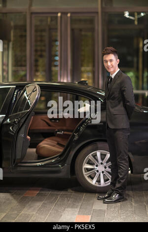 Chauffeur apertura porta auto per il trasporto di passeggeri Foto Stock