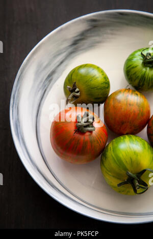 Cimelio di freschi pomodori in un bianco e grigio ciotola in marmo su sfondo nero Foto Stock