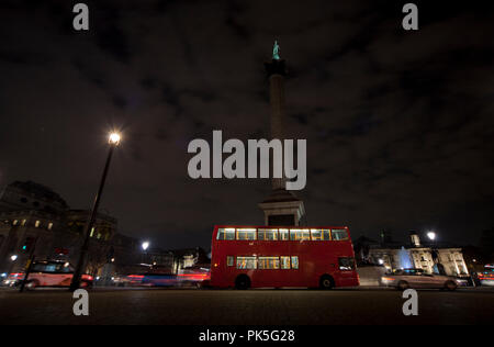 Nelsons Column di notte con il traffico. Una lunga esposizione del traffico che attraversa il fondo della colonna di Nelson, Extreme ampio angolo. Bus rosso e nero con taxi. Foto Stock