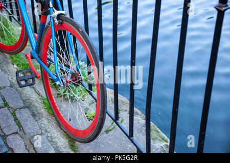 Bicicletta con blu brillante telaio e ruote rosse appoggiata contro la ringhiera accanto a un canale. Foto Stock