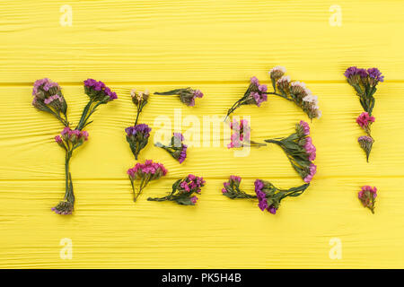 Parola sì fatta di fiori statice. Vista dall'alto. Legno giallo superficie di tavola di sfondo. Foto Stock