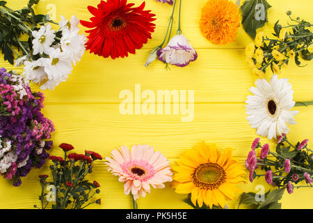 Luminose coloratissimi fiori diversi disposti intorno a. Legno giallo sfondo scrivania. Foto Stock