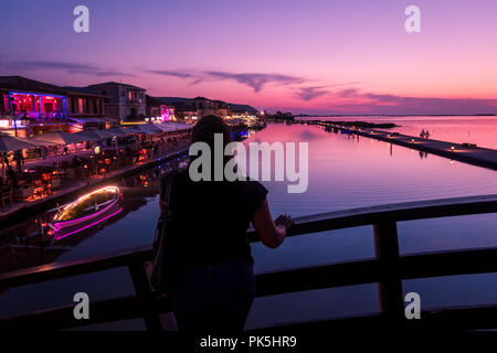 Donna turistica, con ritorno alla macchina fotografica, guardando il tramonto sul ponte del porto a Lefkada (Lefkas), Grecia Foto Stock