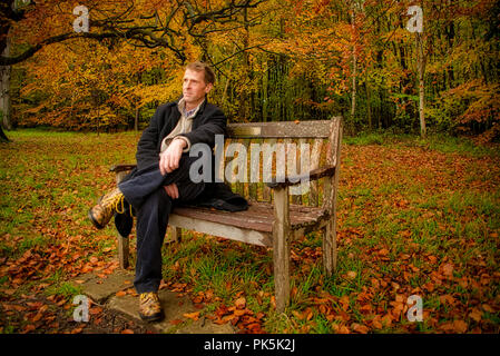 Un uomo in abiti invernali si siede e si rilassa su una panchina nel parco Foto Stock