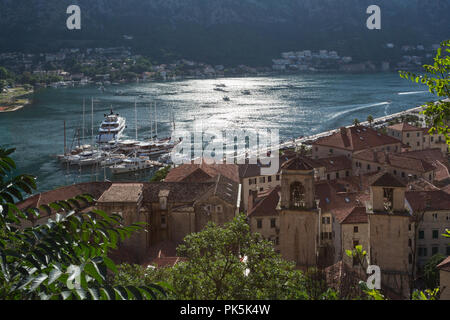 Vista in elevazione della storica medioevale della città murata di Kotor in Montenegro che mostra le barche / yacht nel porto e sun riflettendo sulle acque della baia. Foto Stock