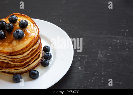 Pancake con mirtilli e miele su sfondo nero, vista laterale. Copia dello spazio. Foto Stock