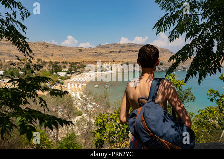 Viaggiare caucasian visto da dietro con zaino guardando una baia blu e acque turchesi su un isola greca in Grecia. Foto Stock