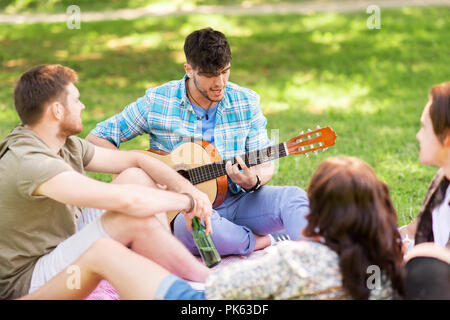 Amici a suonare la chitarra al picnic nel parco di estate Foto Stock