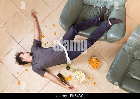 Giovane uomo dopo heavy partying a casa. Un sacco di birra e cibo spazzatura Foto Stock