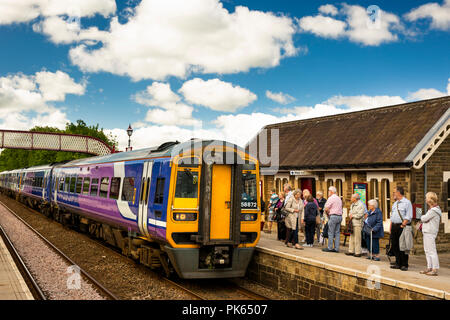 Regno Unito, Yorkshire, Settle, passeggeri sulla stazione ferroviaria in attesa della piattaforma per stabilirsi a Carlisle Linea ferroviaria treno nella luce del sole Foto Stock