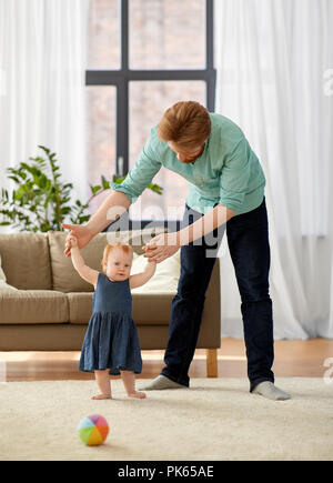 Baby girl in piedi con padre aiutare a casa Foto Stock