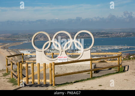 Una scultura in pietra di anelli olimpici sulla isola di Portland contro uno sfondo di Portland Harbour. Gli anelli sono stati scolpiti per celebrare Weymouth e Foto Stock