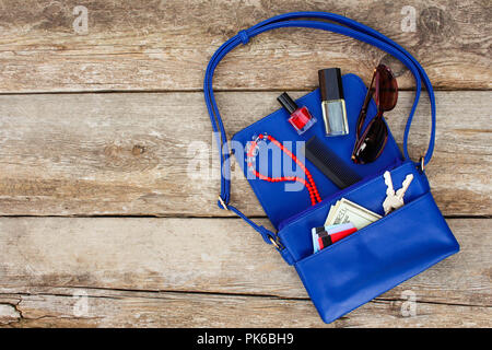 Cose da aprire lady borsa. Cosmetici, soldi e donna accessori è caduto fuori borsa blu. Vista dall'alto. Foto Stock