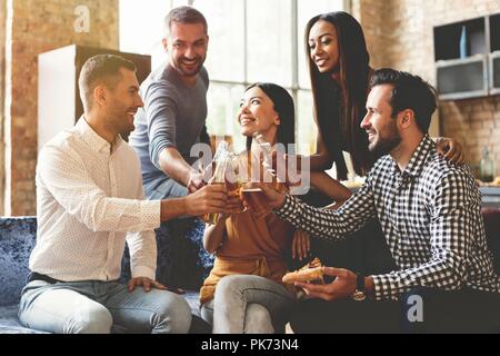Trascorrere molto tempo con i migliori amici. Il gruppo di allegro giovani gustando cibi e bevande mentre trascorrere del tempo piacevole nel confortevole sedie sulla cucina insieme. Foto Stock